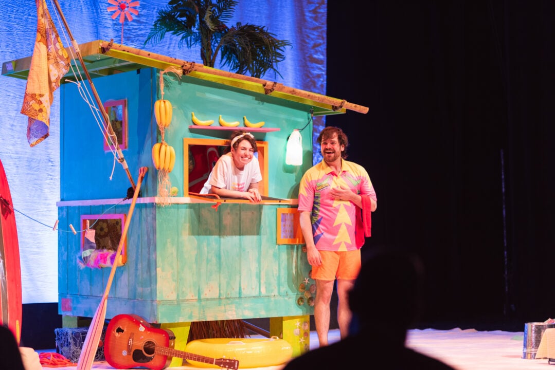 Two people standing on a stage with a colourful house