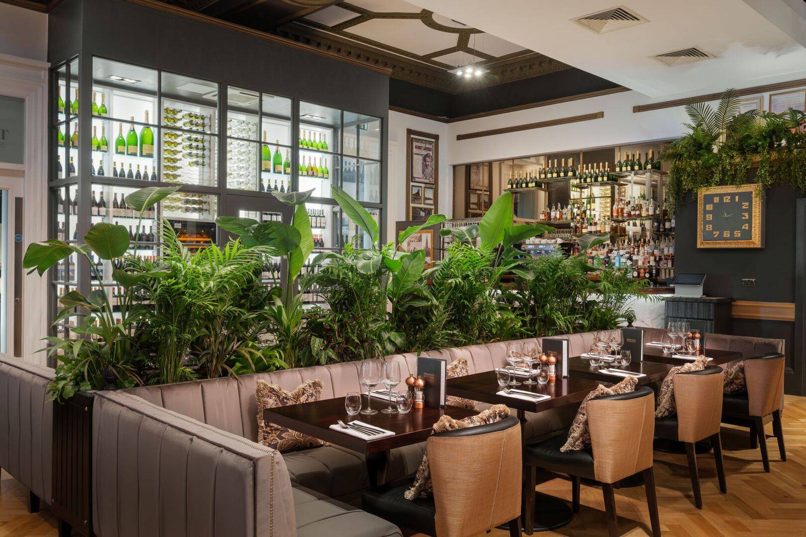 Row of tables with foliage behind with large wine display in the background