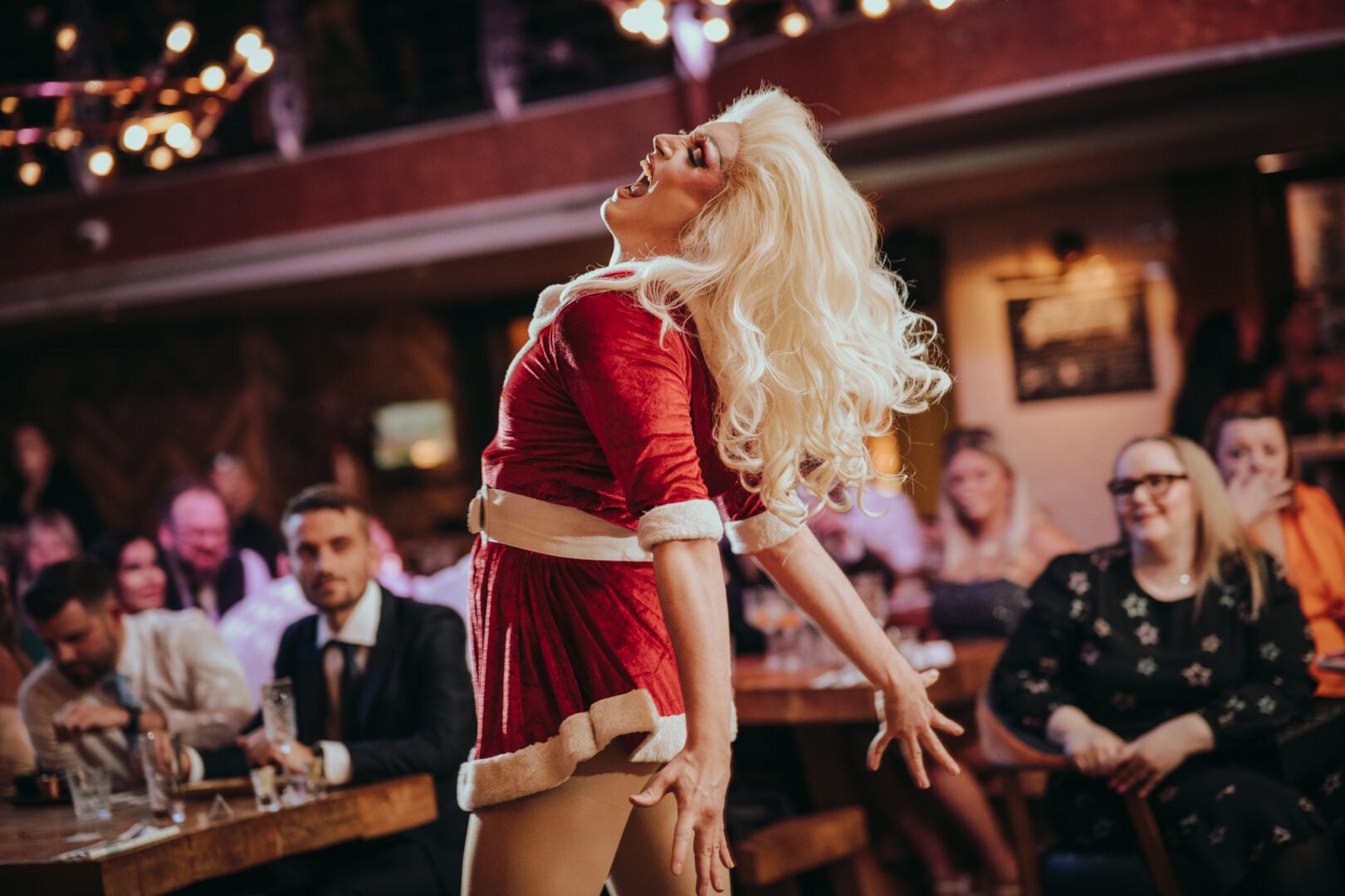 A person dressed in a red and white Santa dress, dancing in front of an audience.