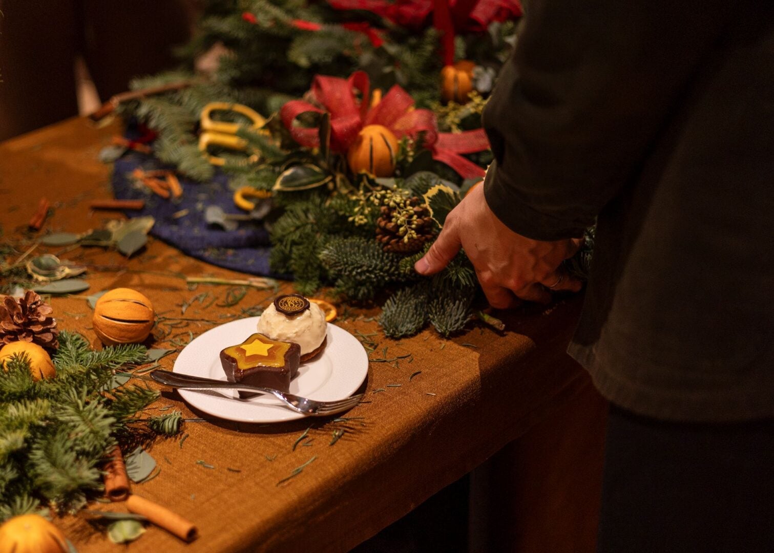 Close-up of a Christmas wreath being made, along a plate with 2 cakes.